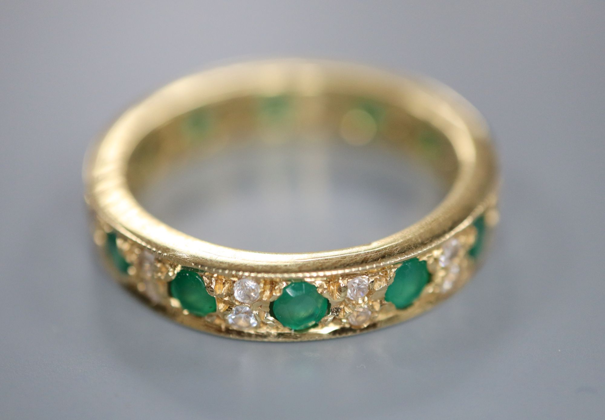 A mid to late 20th century yellow metal, emerald and diamond set full eternity ring, size P/Q, gross 5.7 grams.